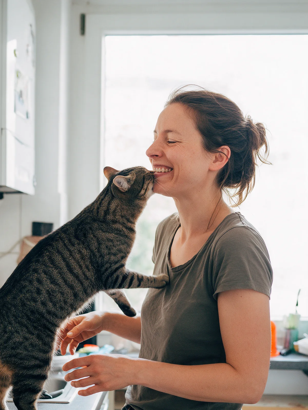 Eine Frau lacht in ihrer Küche, während ihre Katze sich an ihrem Kinn reibt